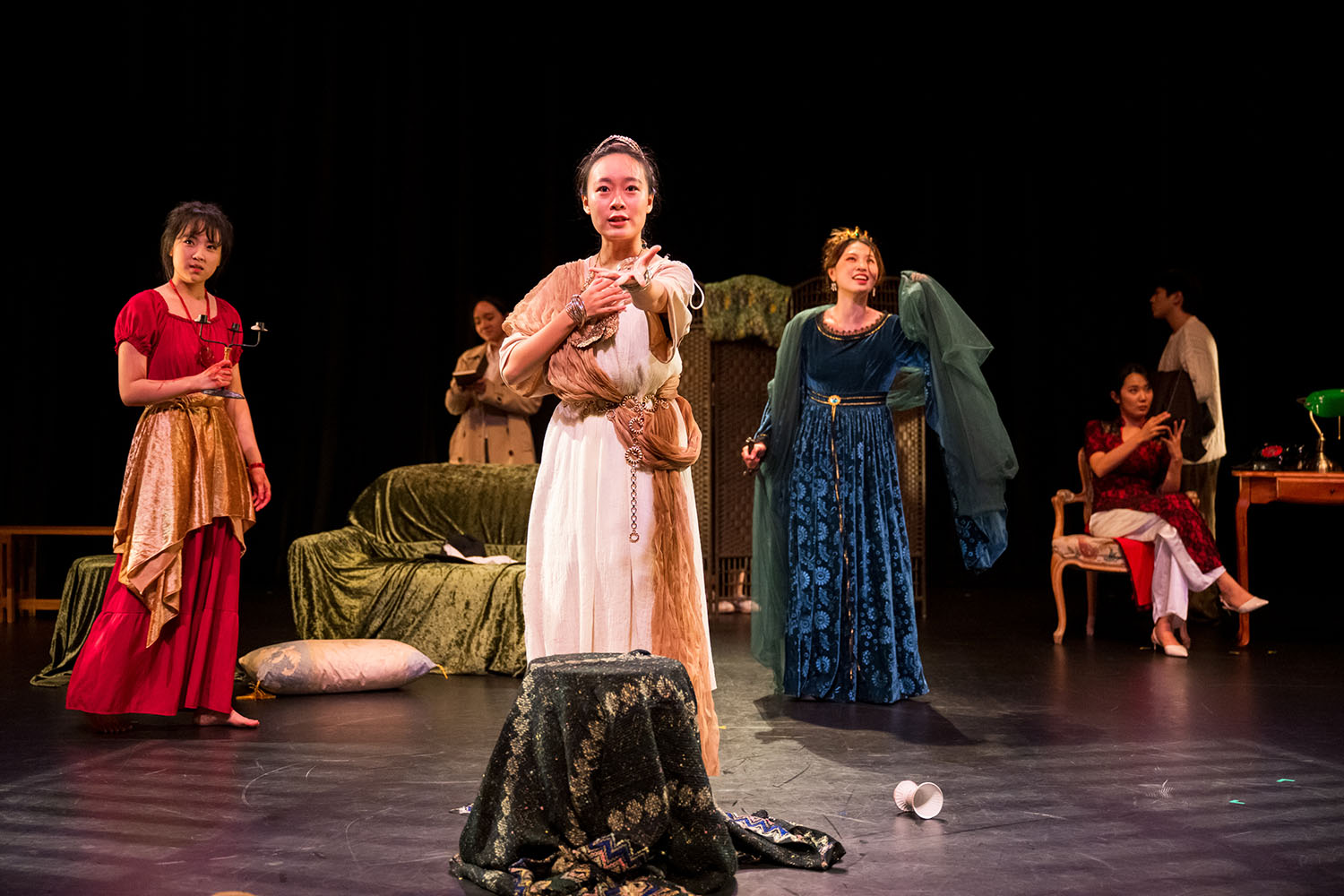 Various performers, predominantly female, dressed in gowns and robes.