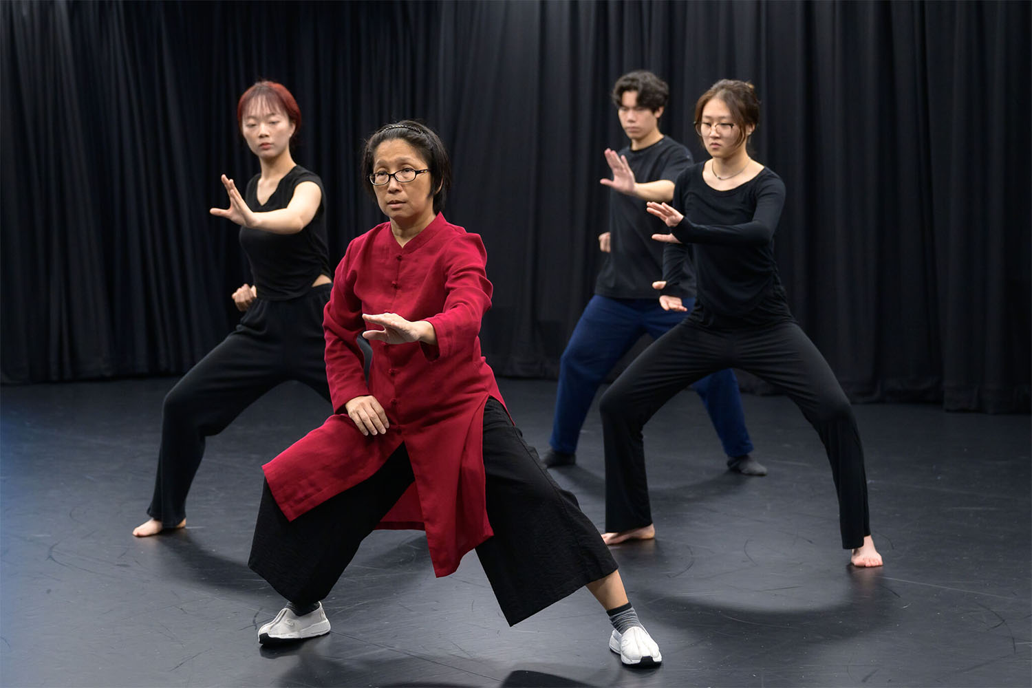 4 performers in wushu stances, the frontmost performer in a red and black robe.