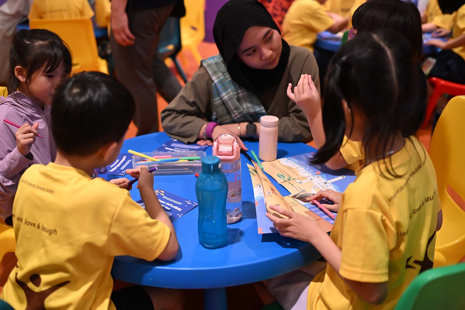 A group of children and a teacher at a table, engaged in creative activities such as crossword puzzles with paper and pencils.