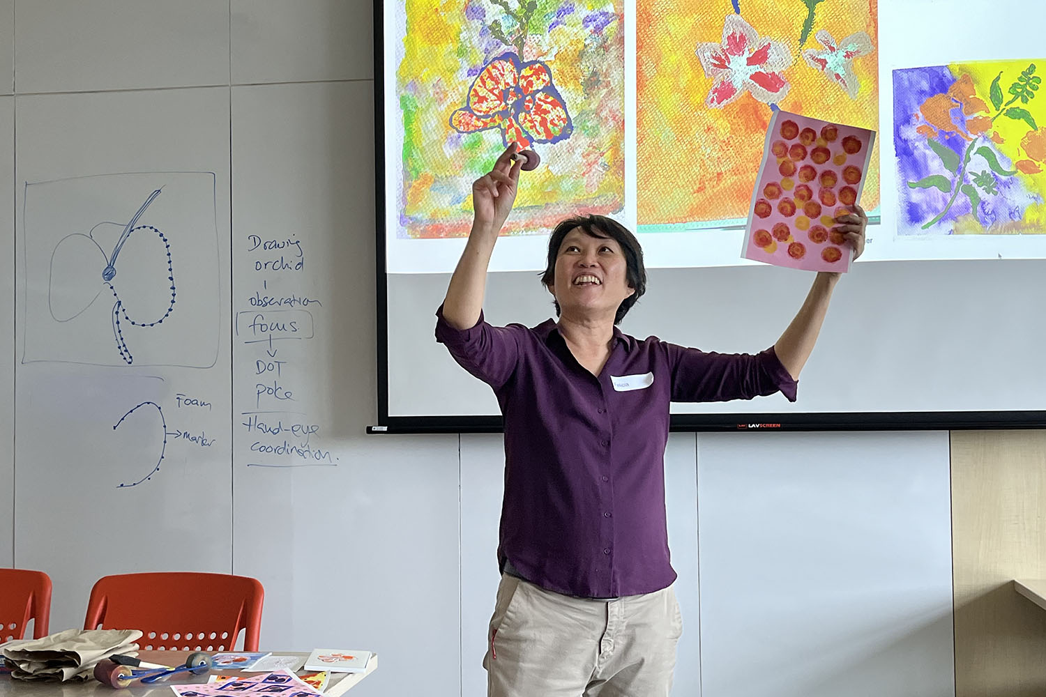 A female presenter holding a painted paper teaching the attendees how to paint an orchid.