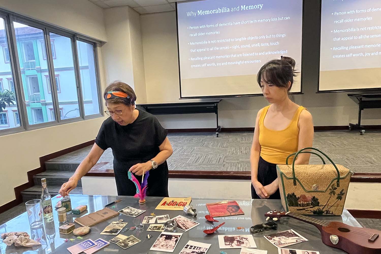 Two female presengers presenting with a table of various photos and objects on why memorabilia is important for the elderly especially those with dementia.