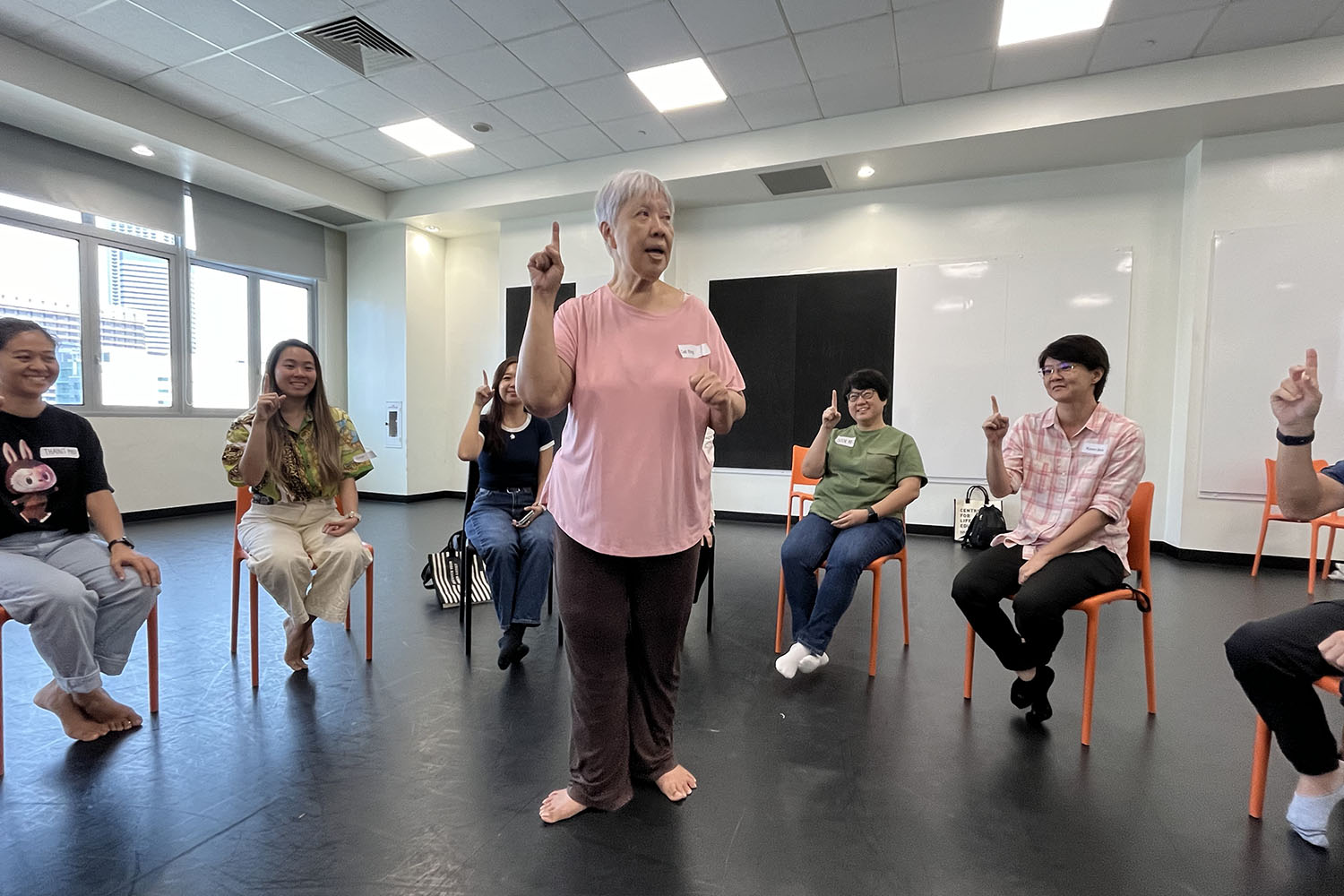 An elderly woman in the center with various adults seated in a circle doing a group talking activity.
