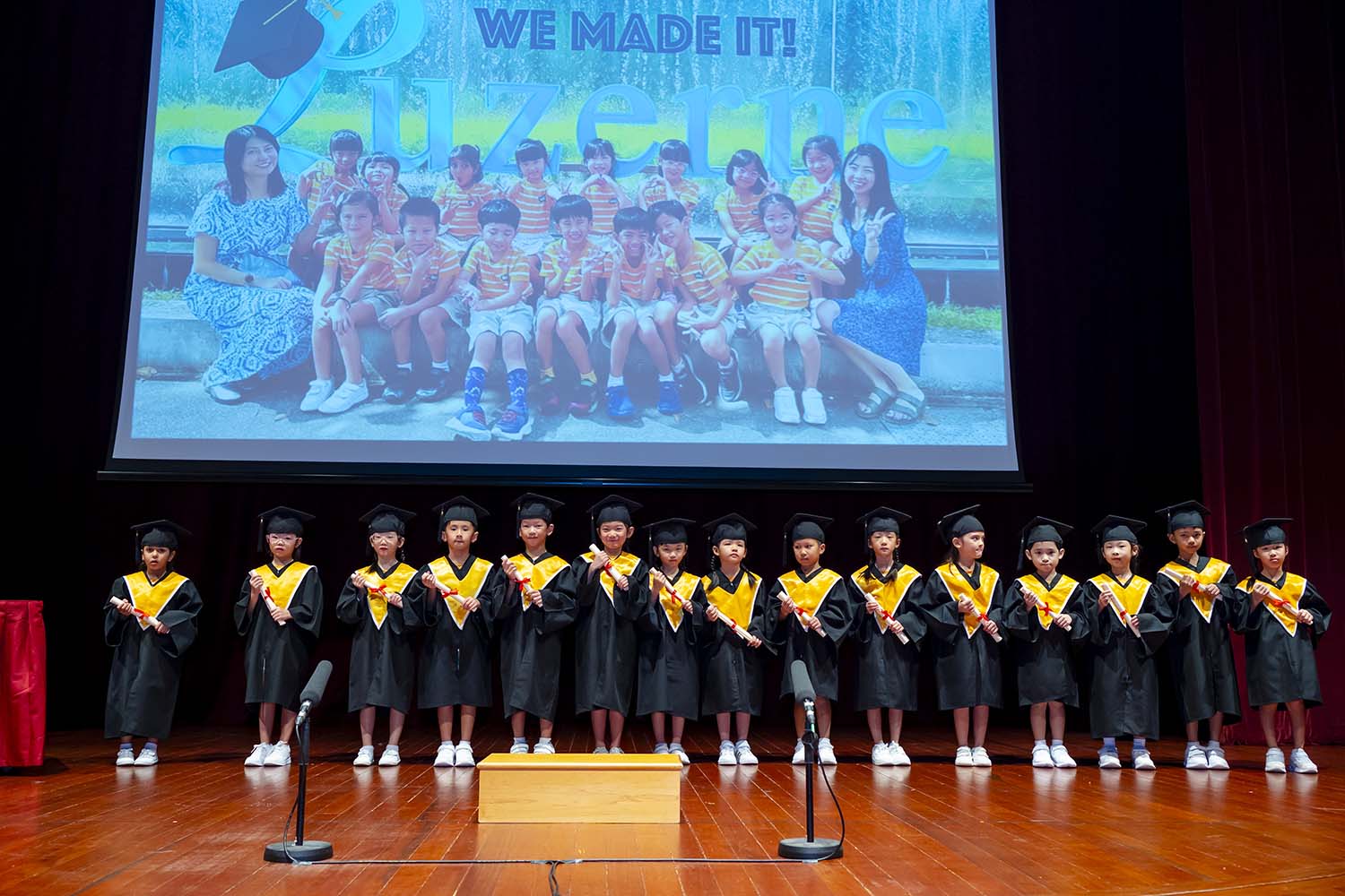 Various preschool K2 young learners in graduation gowns on stage.