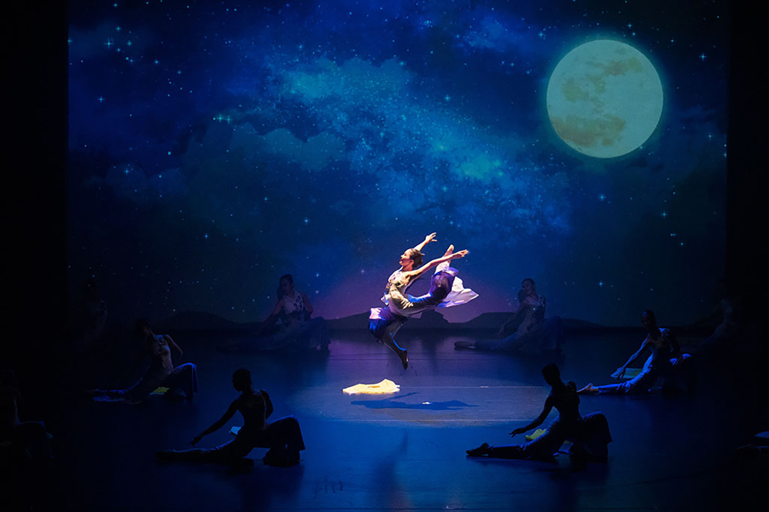 All-female dance performance in a dimly-lit dark blue stage representing night time with a moon.