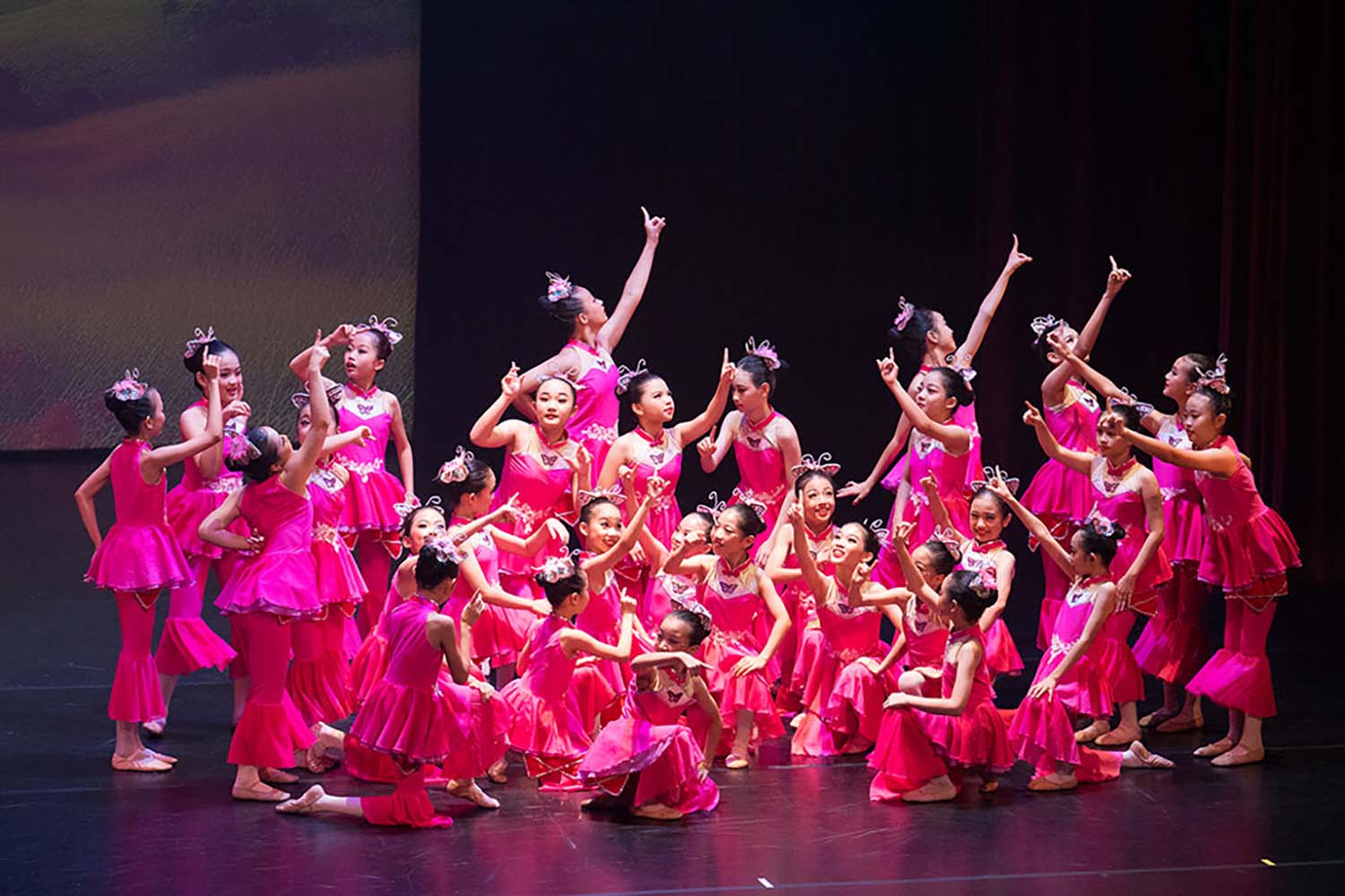 Junior Dance performers, females, in vibrant Chinese magenta/pink folk gowns.