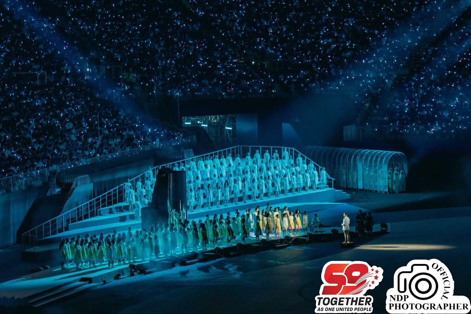 NDP59 various performances in lumiscent yellow suits performing on parade under dark blue light at night.