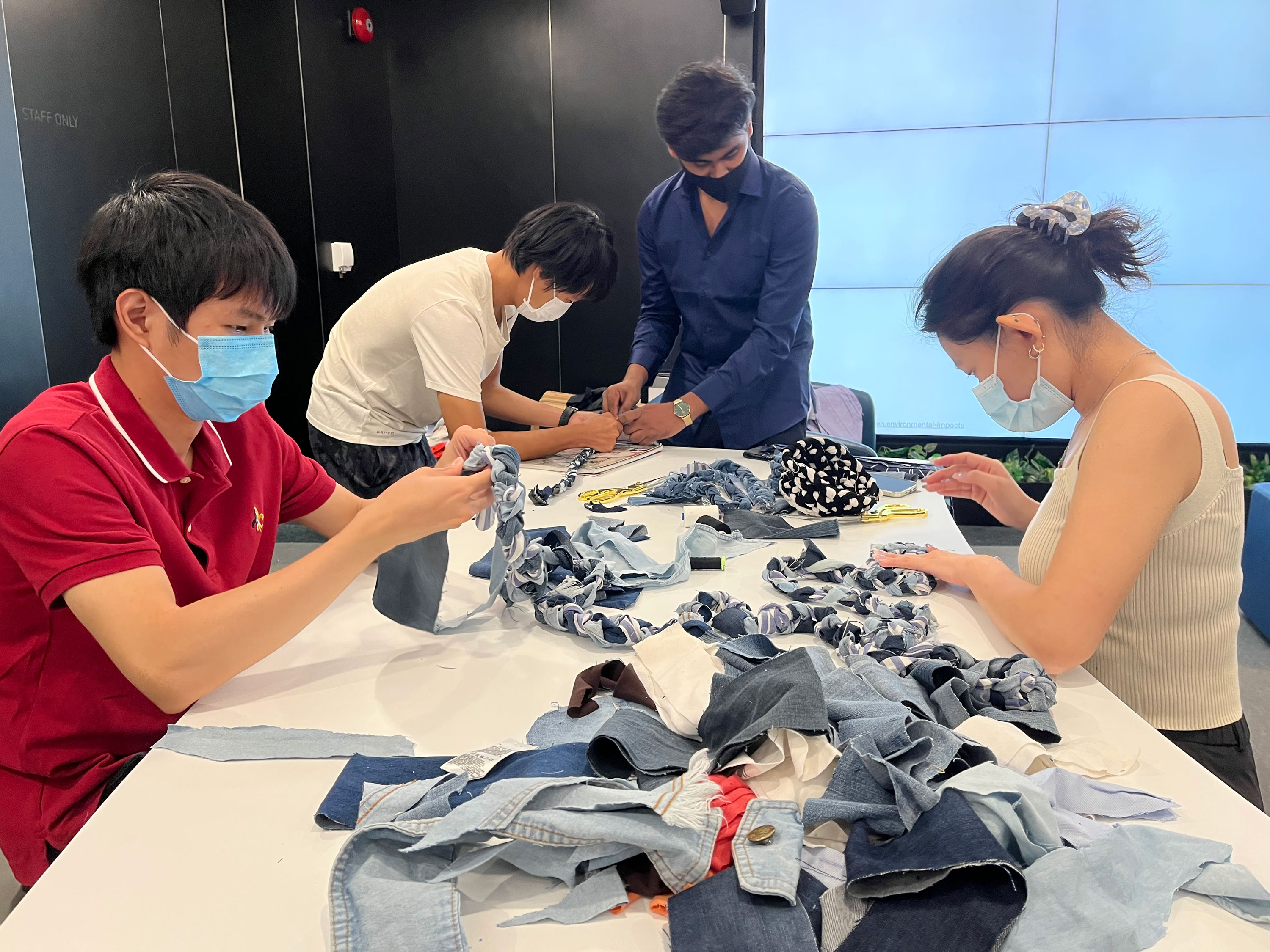 Participants of the workshop braiding cut denim strips in preparation to make a container